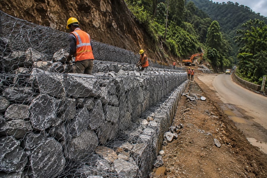 Gabion retaining wall under construction along a hillside road